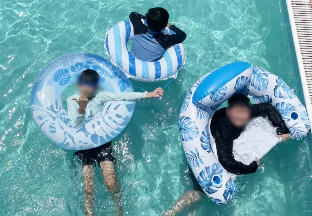 3人のこどもが浮き輪で泳いでいる